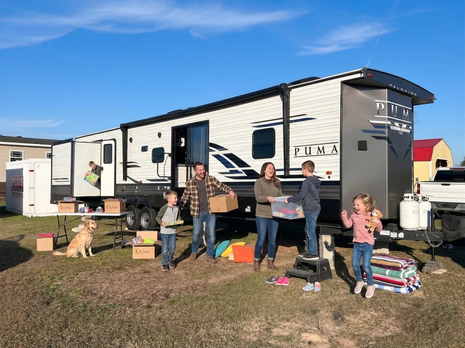 A family unloading their belongings into a delivered travel trailer with their dog